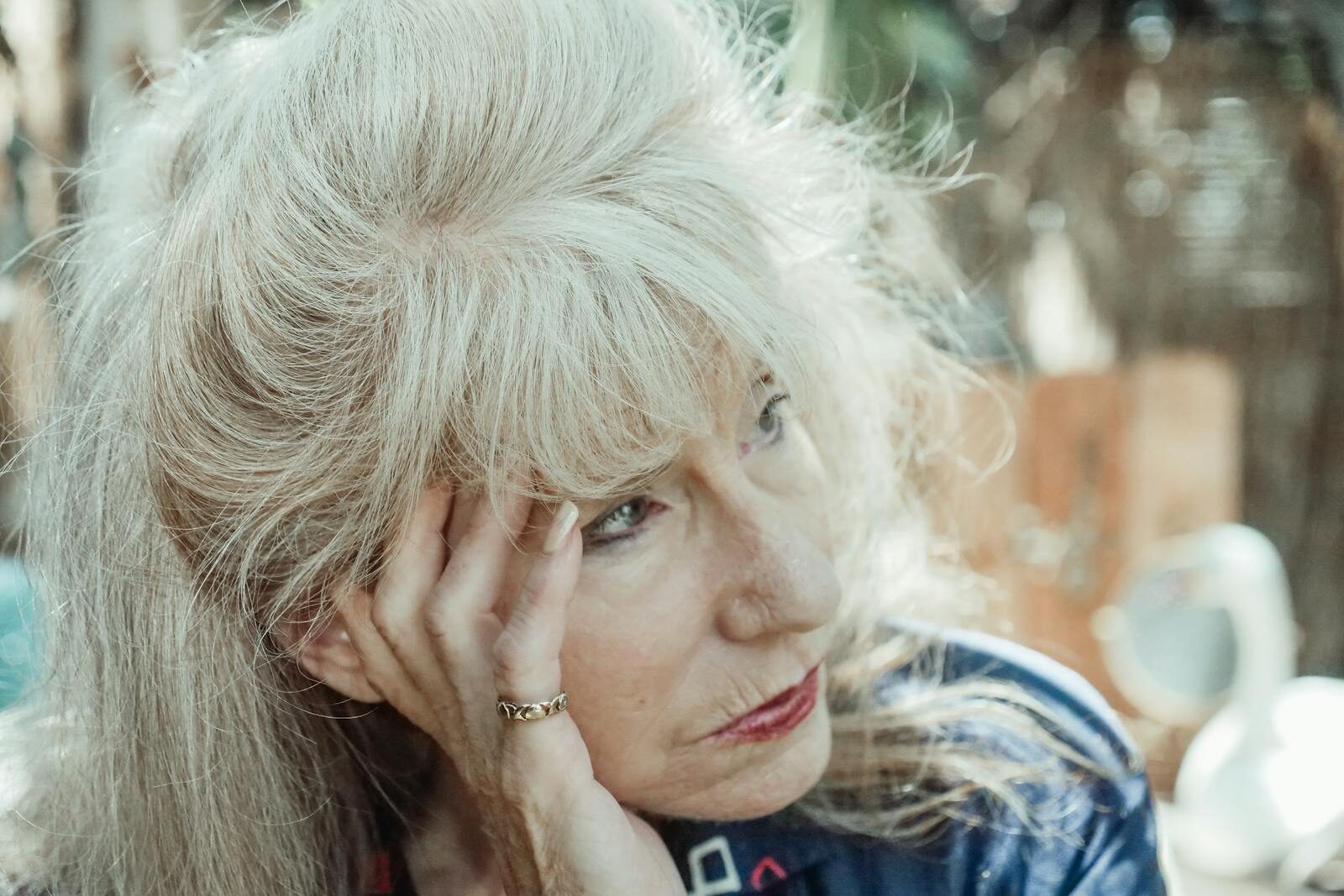 An introspective senior woman in thought, sitting outdoors on a sunny day.